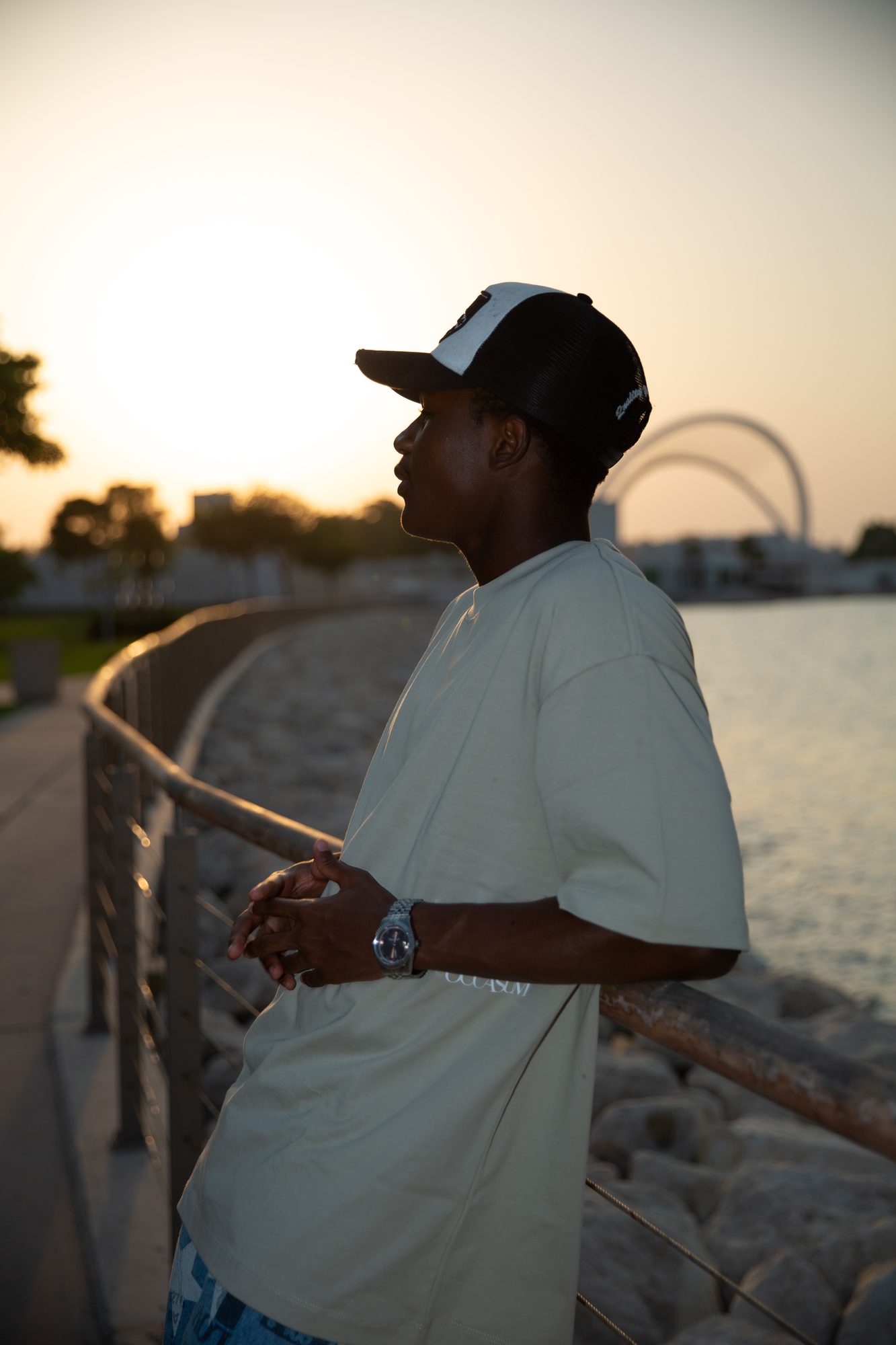 Model in a cap leaning on a rail at sunset