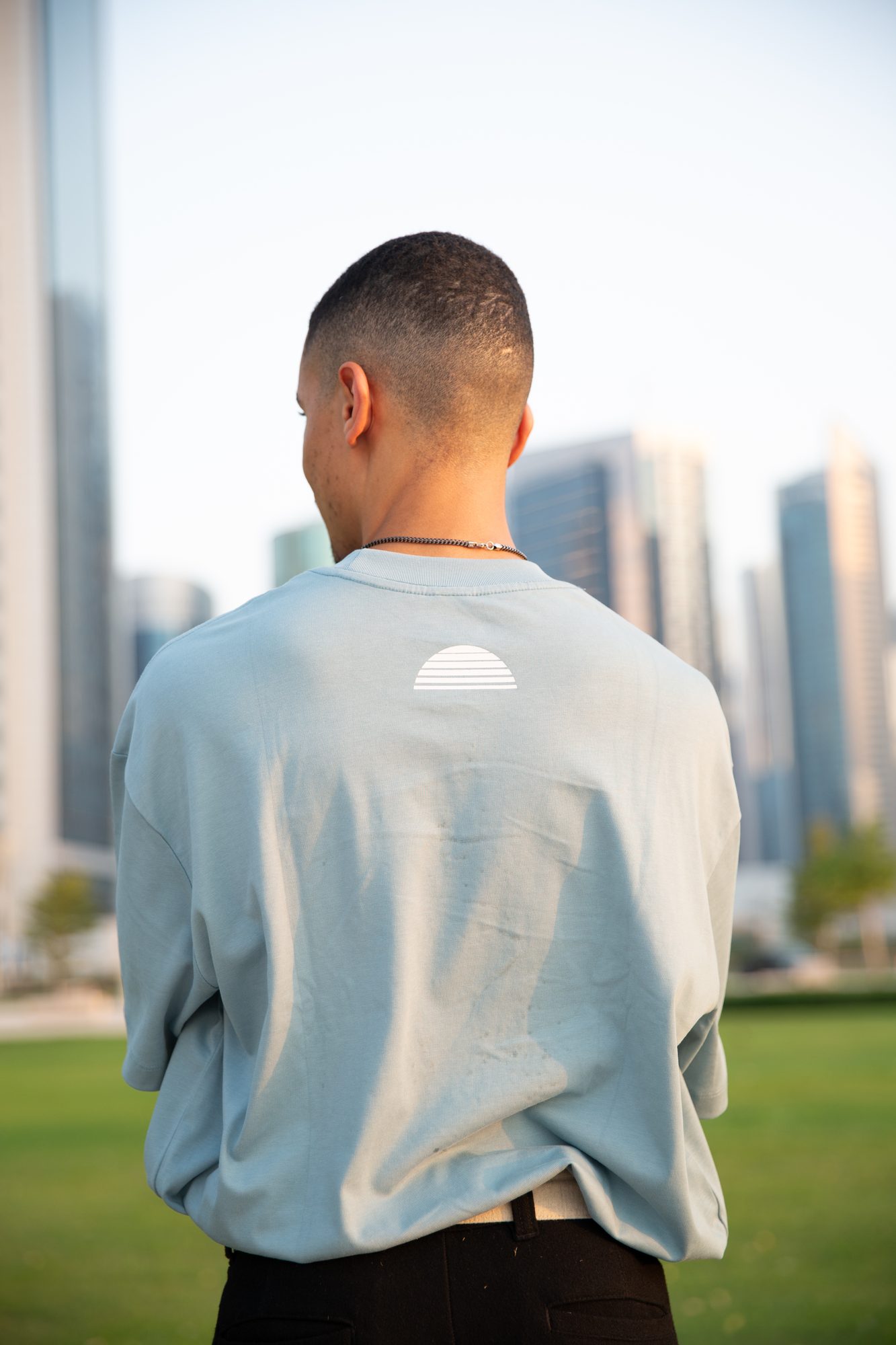 Back of a haze blue OCCASUM tee with the sunset mark